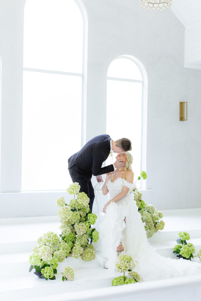 Bride and groom in white chapel with greenery and hydrangeas