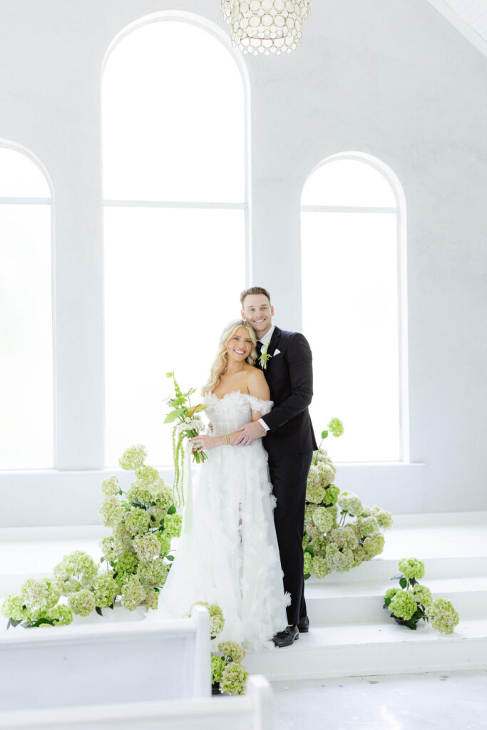 Bride and groom in white chapel with greenery and hydrangeas