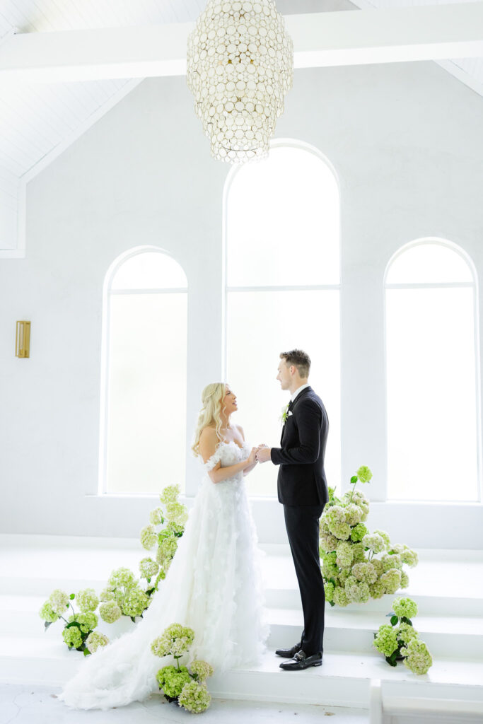 Bride and groom in white chapel with greenery and hydrangeas