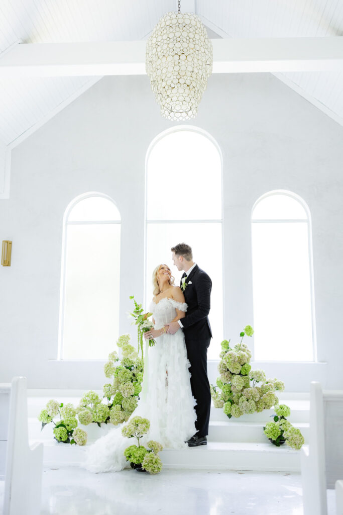 Bride and groom in white chapel with greenery and hydrangeas