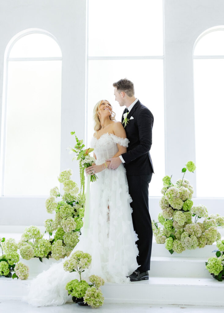 Bride and groom in white chapel with greenery and hydrangeas