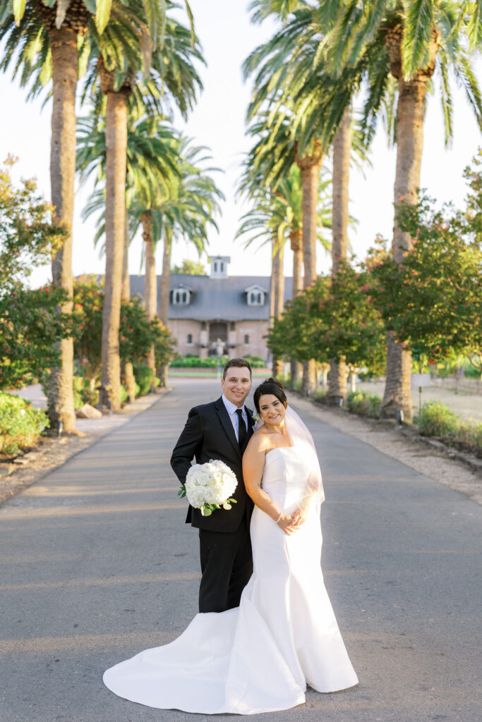 Couple walking hand in hand along palm tree lined driveway at The Palm Event Center