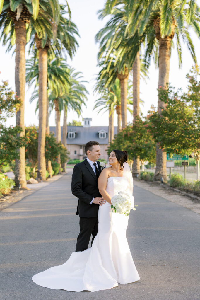 Couple walking hand in hand along palm tree lined driveway at The Palm Event Center