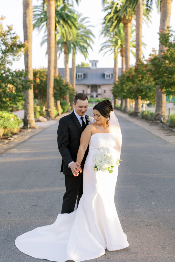 Couple walking hand in hand along palm tree lined driveway at The Palm Event Center